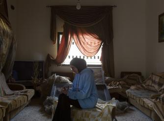 A young woman from Lebanon looks at a family photo album in her living room, which was damaged after it was bombed by Israeli forces. 